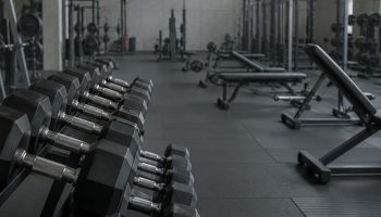 A rack of dumbbells in the foreground of a quiet gym floor early in the morning