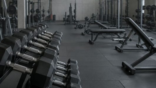 A rack of dumbbells in the foreground of a quiet gym floor early in the morning