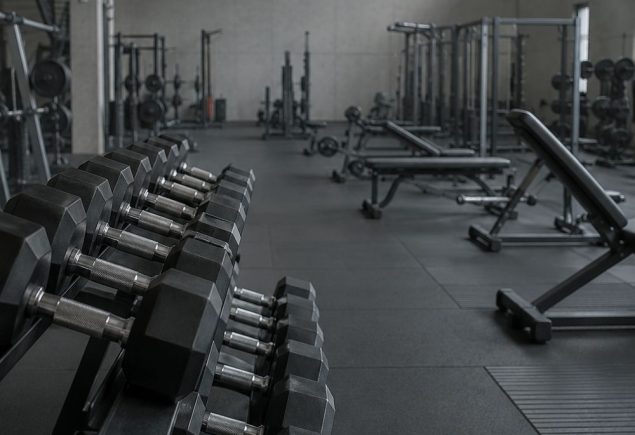 A rack of dumbbells in the foreground of a quiet gym floor early in the morning