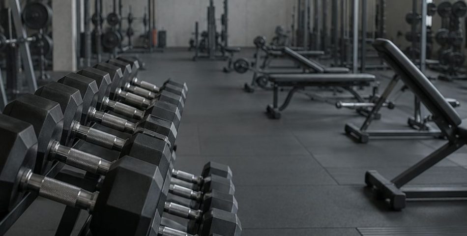 A rack of dumbbells in the foreground of a quiet gym floor early in the morning
