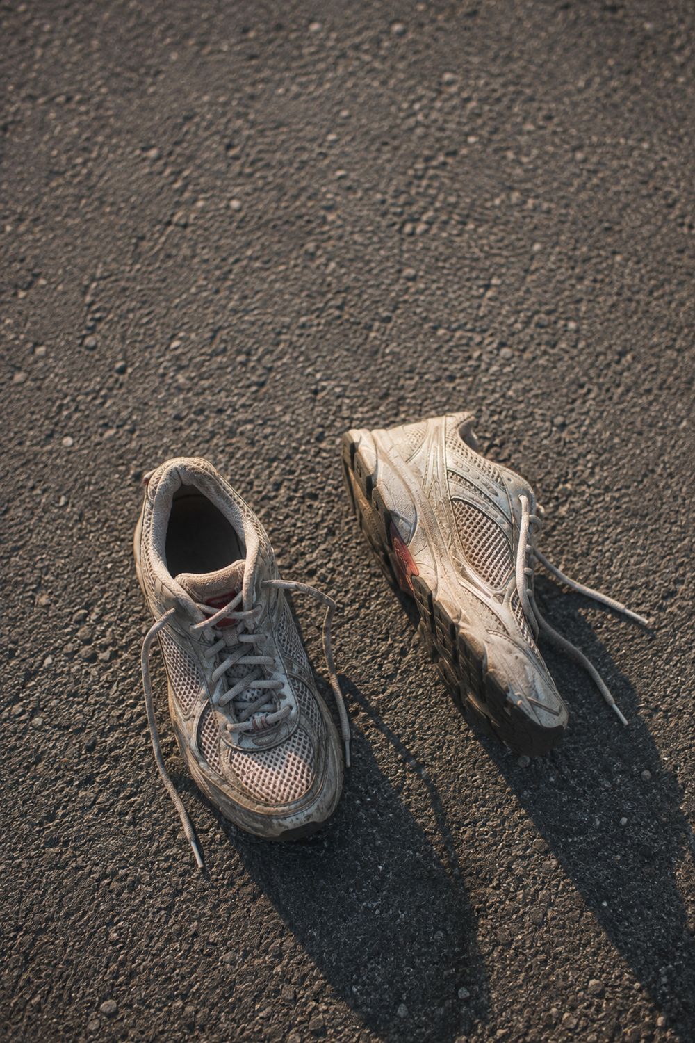 A pair of neutral running shoes on a worn tarmac path in early morning light
