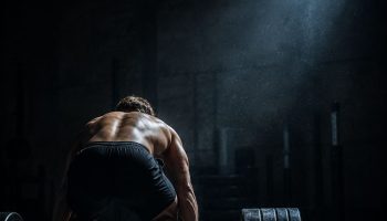 Athlete standing at a loaded barbell in a dark gym at dawn, ready to begin a hybrid training session