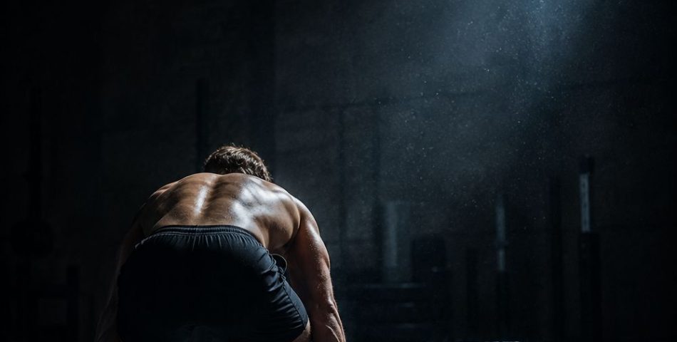 Athlete standing at a loaded barbell in a dark gym at dawn, ready to begin a hybrid training session