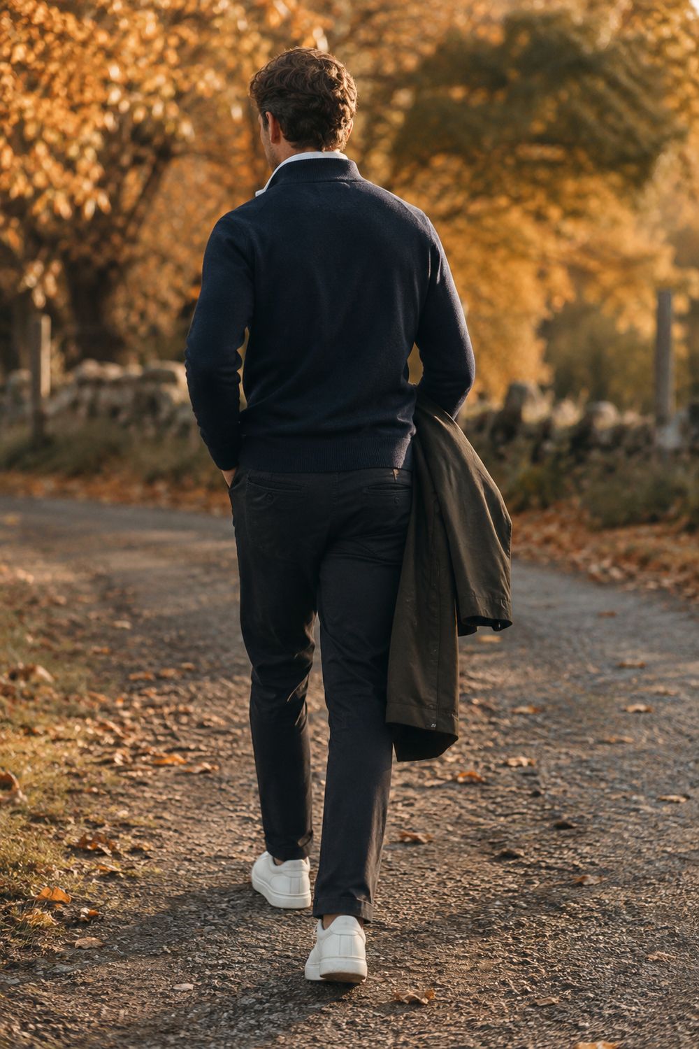 A men’s game day outfit — navy quarter-zip over a collared shirt with dark chinos and white trainers on an autumn path
