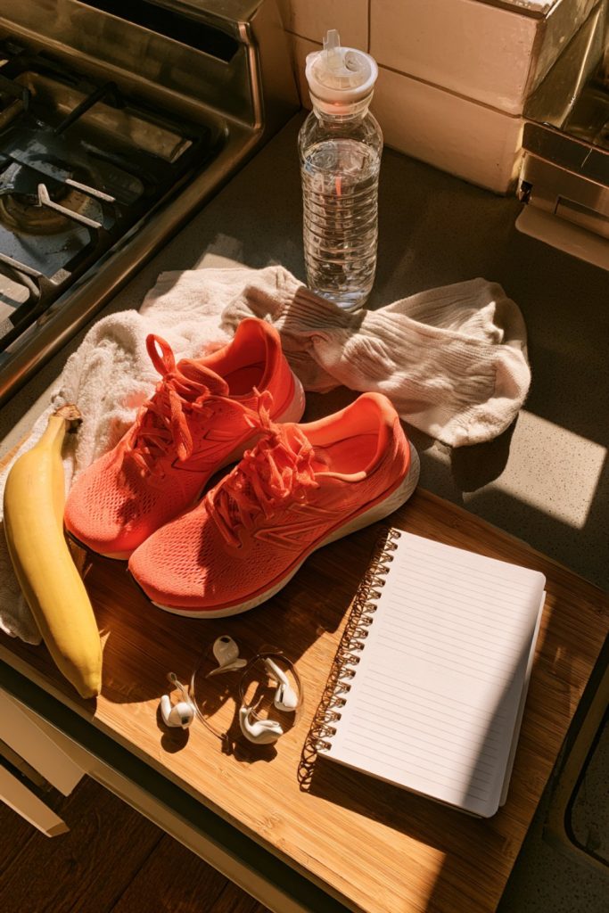 Morning run essentials on a counter: bright running shoes, socks, banana, water bottle and a notebook