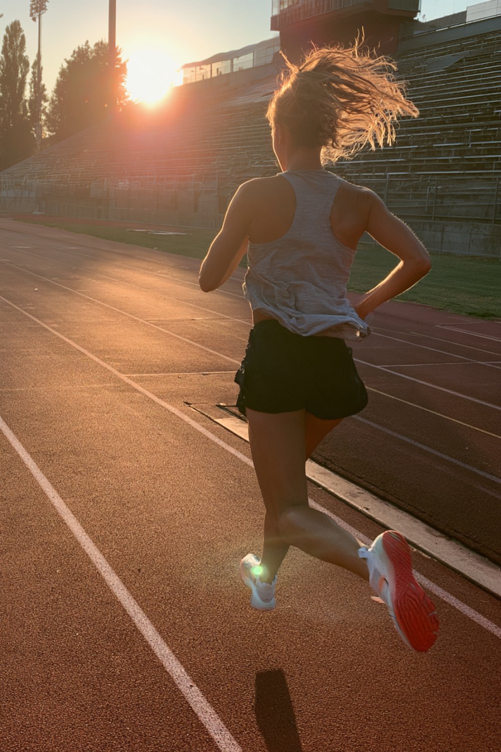 Runner seen from behind doing intervals on a red track at golden hour
