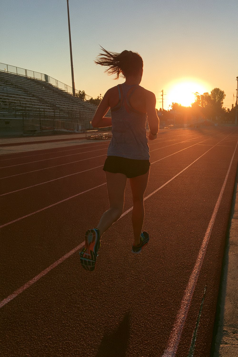 Runner seen from behind striding down the home straight of an outdoor track at sunset