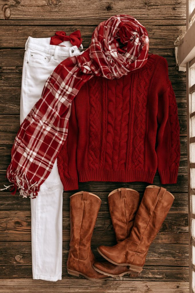 Flat lay of a red sweater, white jeans and red and white plaid scarf on a wooden porch