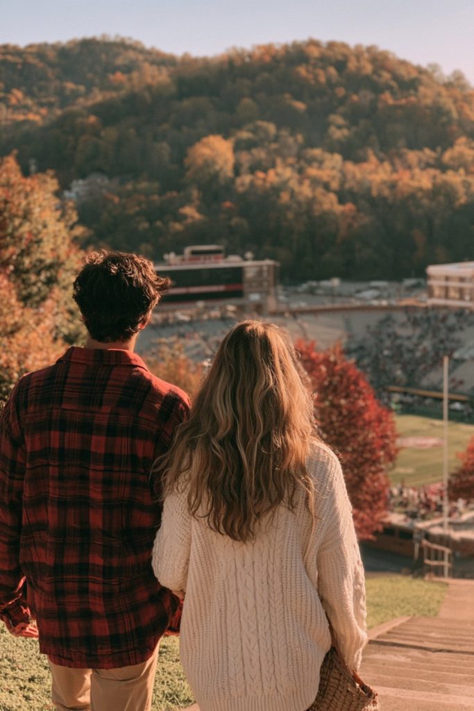 Couple seen from behind looking toward a college stadium in the autumn Ozark hills