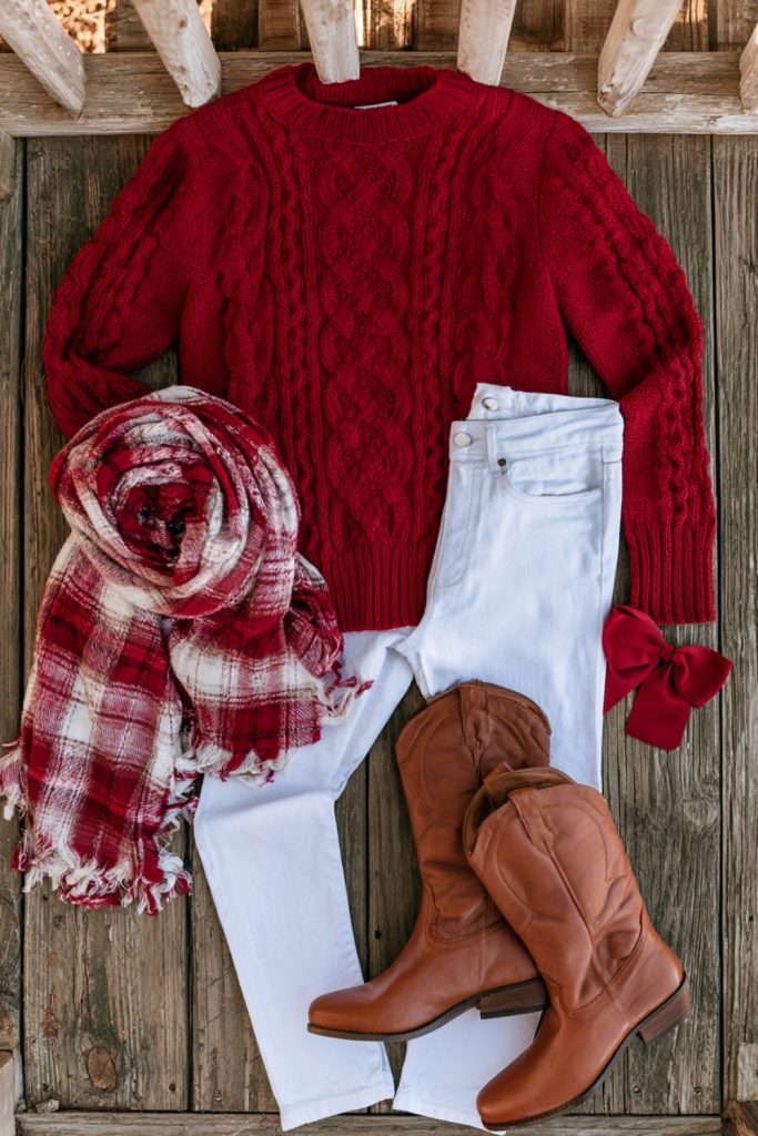 Cardinal red cable knit sweater and white jeans laid out for an Arkansas game