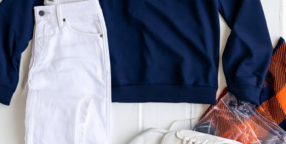 Auburn game day outfits flat lay with a navy quarter-zip, white jeans, orange beanie, white sneakers and a clear stadium bag