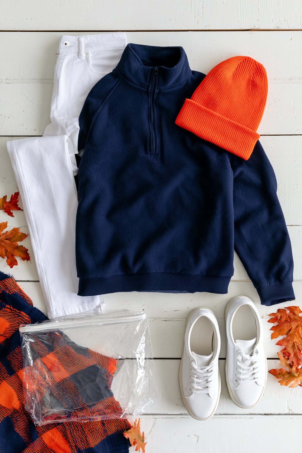 Navy and orange game day outfit with white jeans, orange knit beanie and a navy and orange plaid blanket