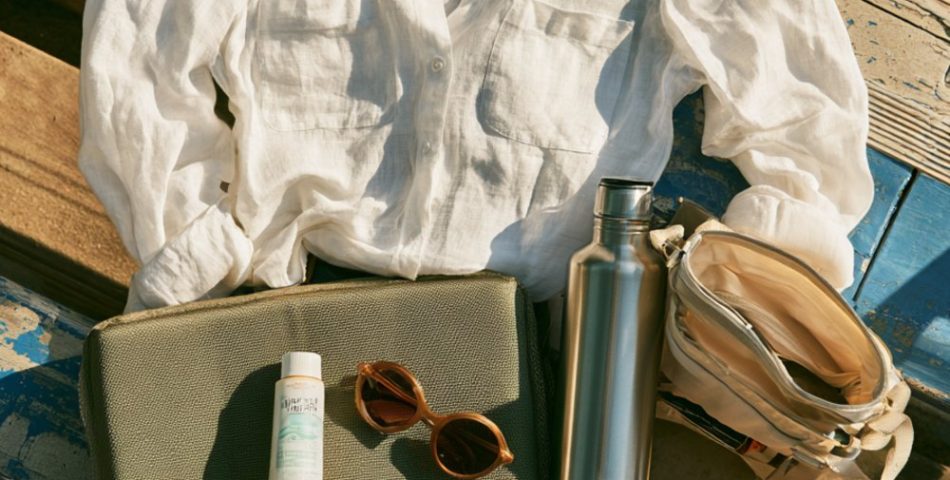 Flat lay on bleacher planks of a navy cap, white linen shirt, denim shorts, sandals, sunscreen and seat cushion