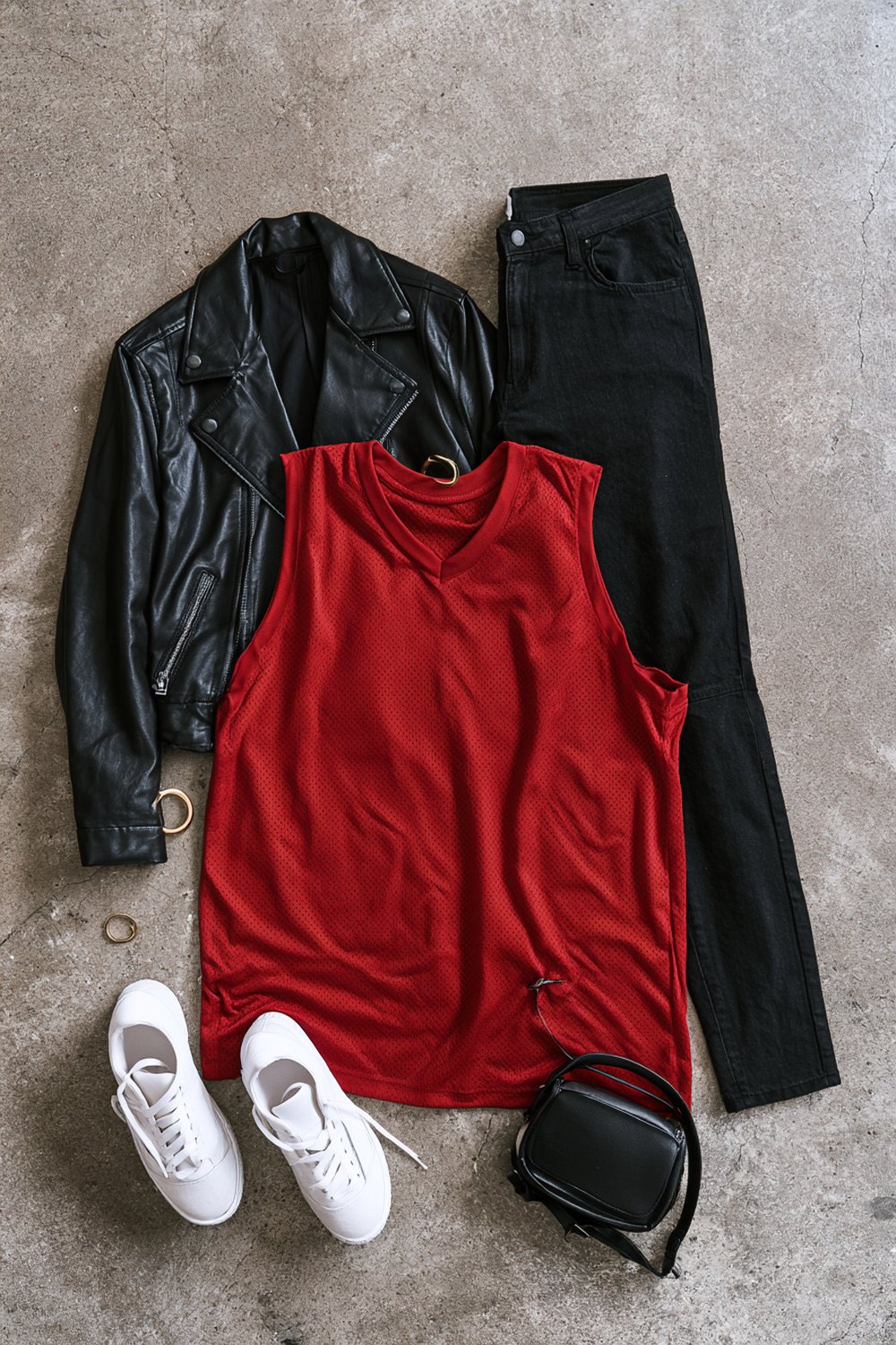Basketball game outfits for women flat lay with a black leather jacket, red mesh jersey top, black jeans, white sneakers and a small black crossbody bag