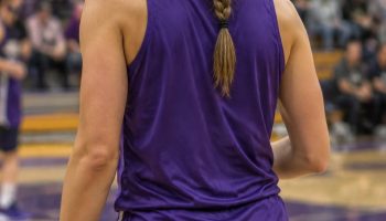 Basketball player seen from behind on a court with a long braided high ponytail and a purple practice jersey