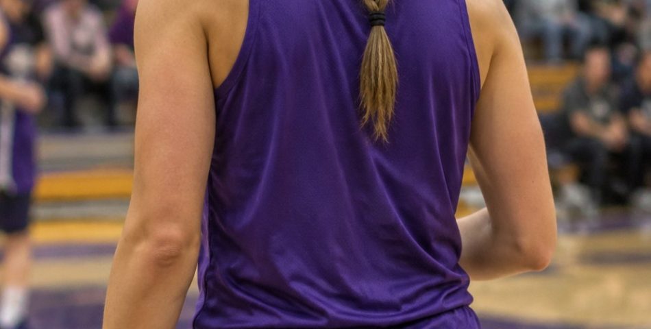 Basketball player seen from behind on a court with a long braided high ponytail and a purple practice jersey
