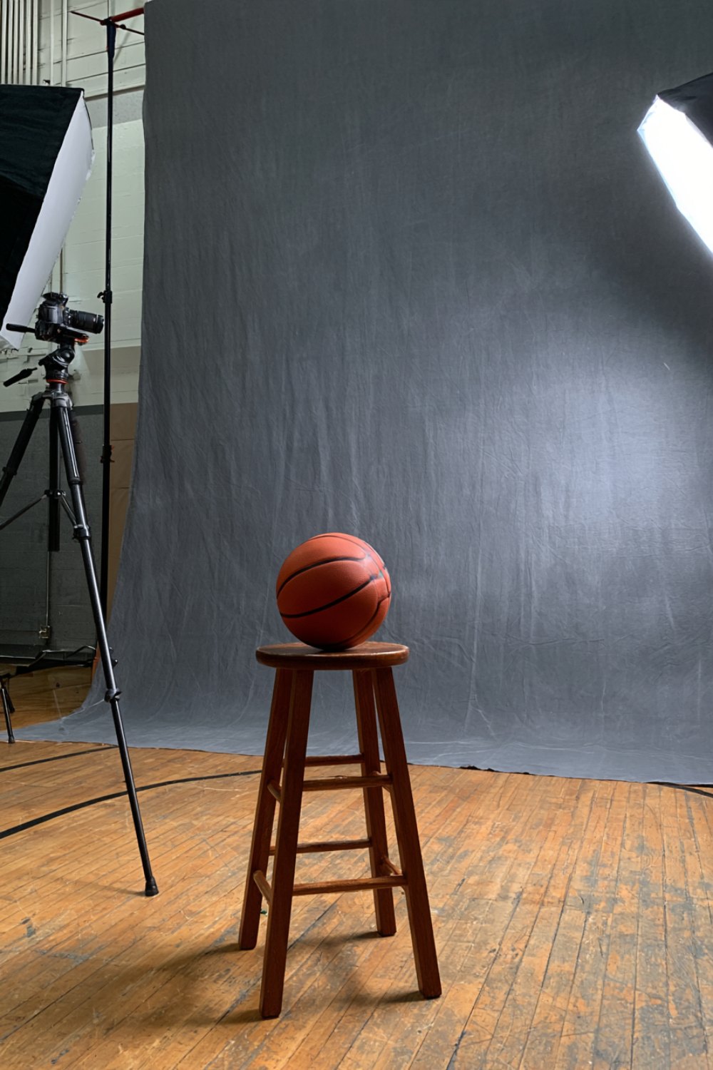 Media day setup in a school gym: grey backdrop, two softbox lights and a basketball on a wooden stool