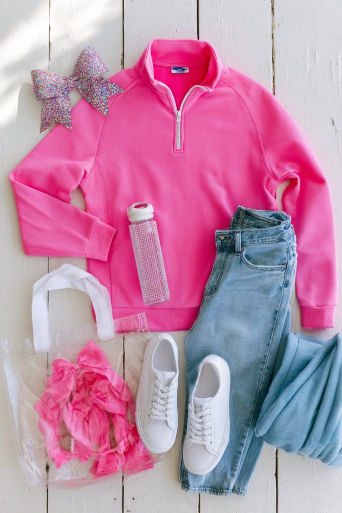 Cozy pink half-zip with jeans, sneakers, water bottle and glitter bow arranged on white wood