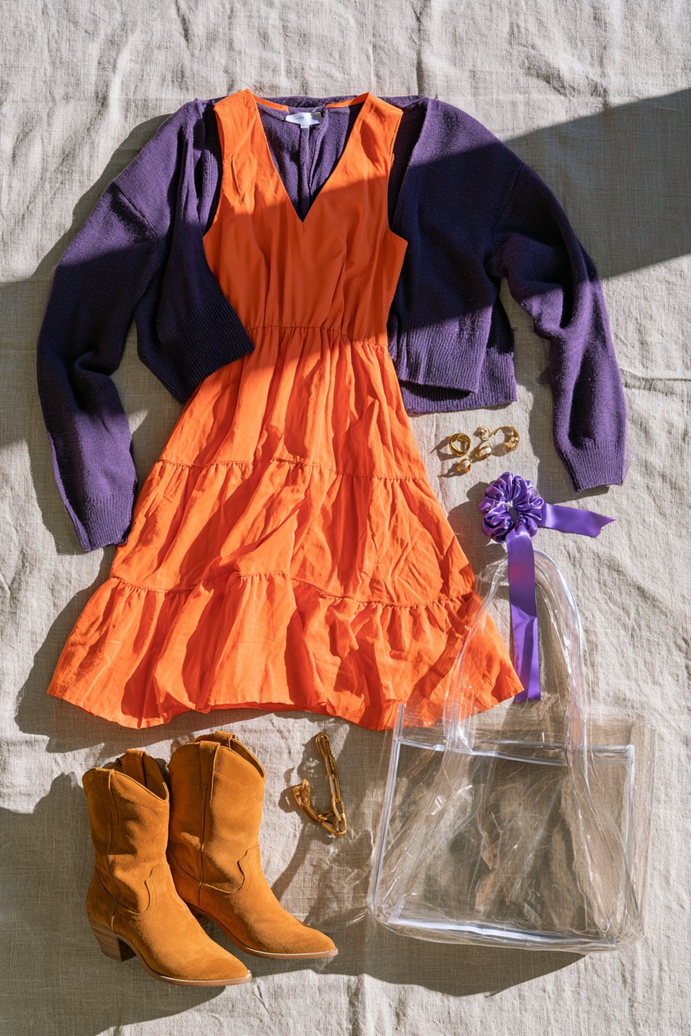 Orange tiered midi dress layered with a purple cardigan and suede cowboy boots