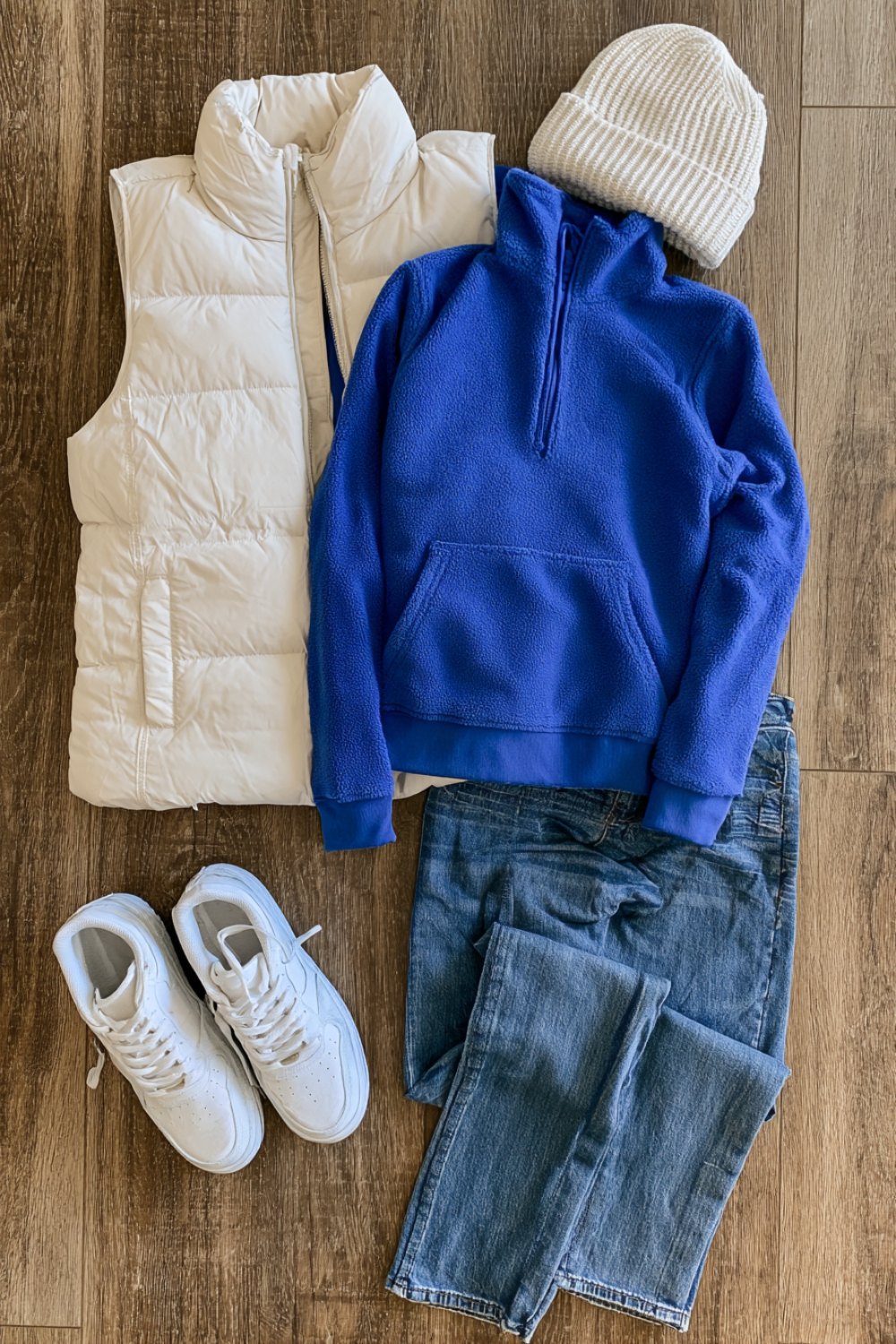 Royal blue quarter zip and white puffer vest with jeans and sneakers laid out for a cold game day