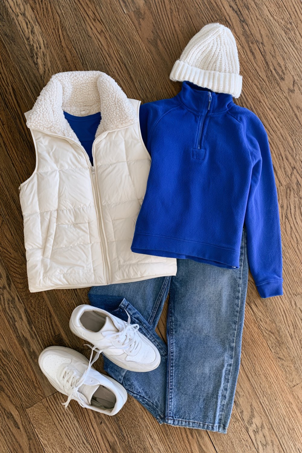 White puffer vest, blue pullover and white beanie flat lay for a winter game