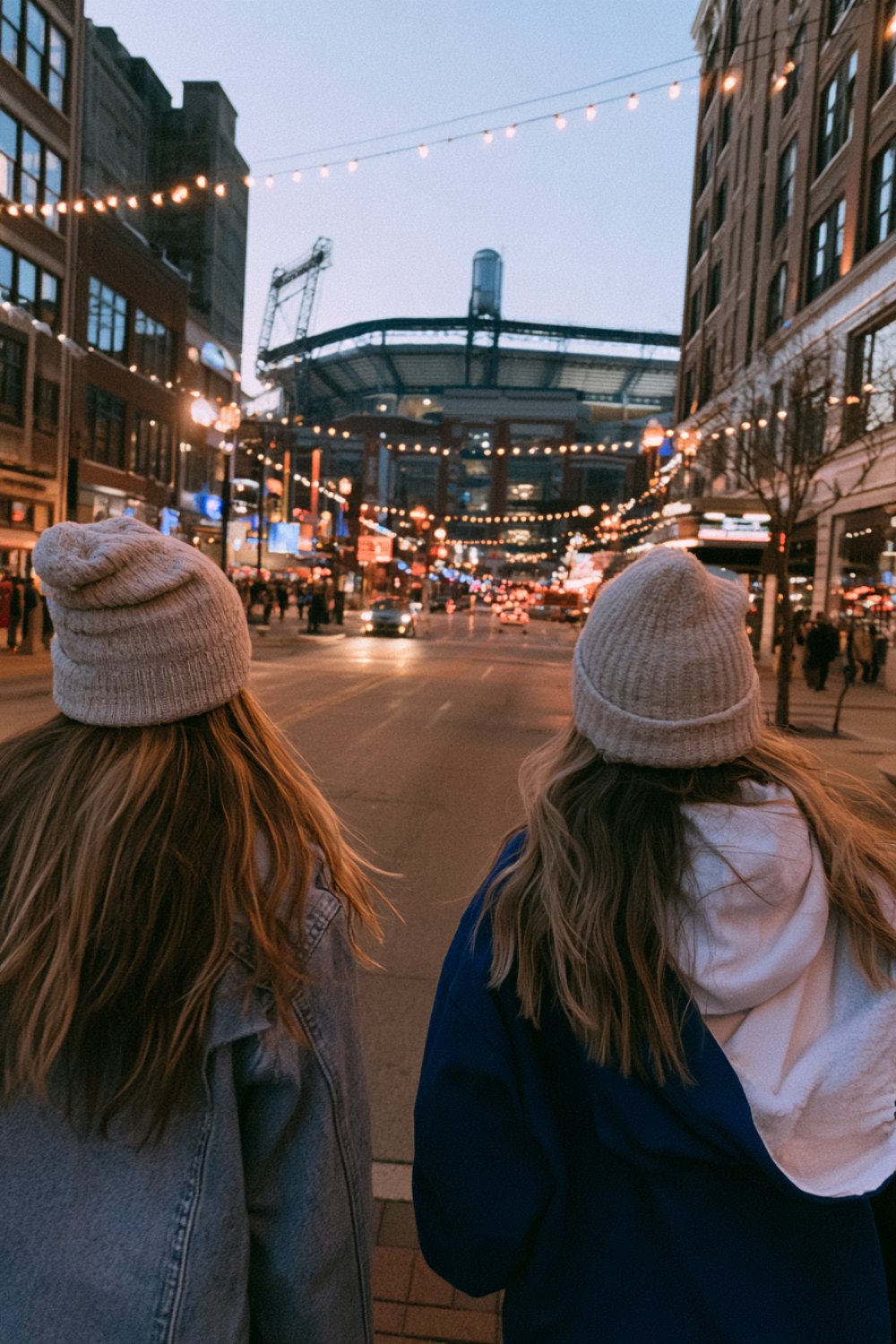 Friends from behind in blue and white layers and knit beanies heading to a night game downtown