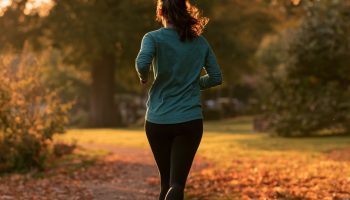 Beginner woman runner jogging on a leaf-covered park path in a teal top and black leggings