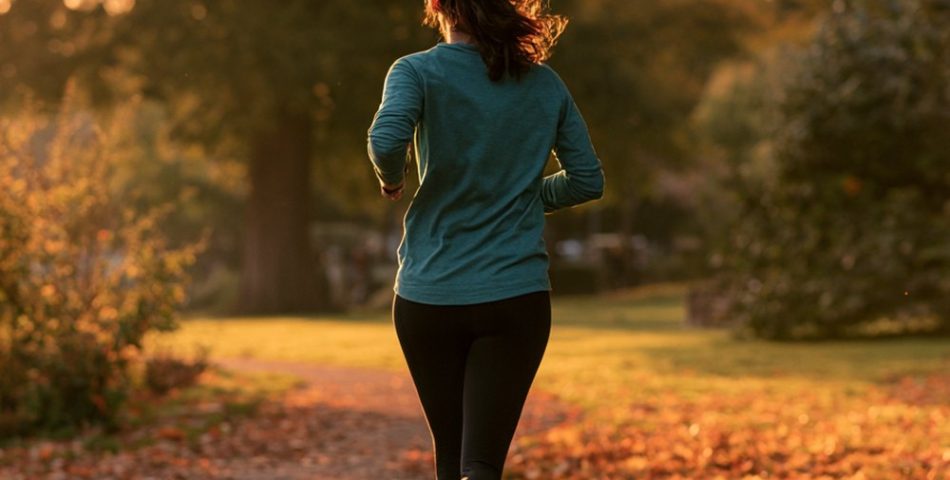 Beginner woman runner jogging on a leaf-covered park path in a teal top and black leggings