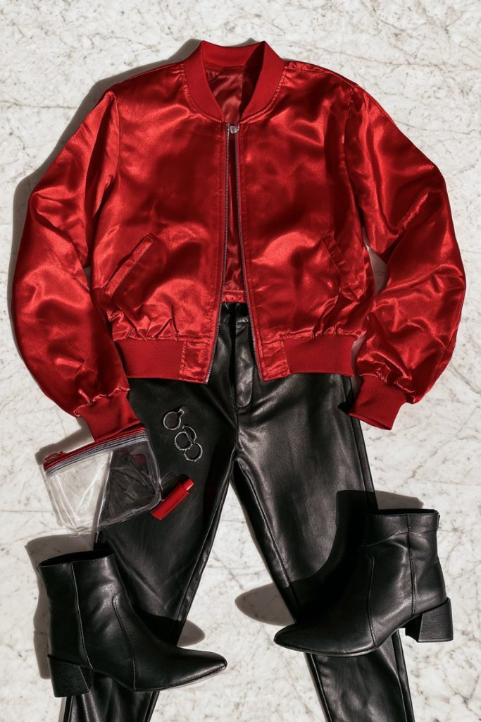 Flat lay of a red satin bomber jacket, black faux leather pants and black ankle boots