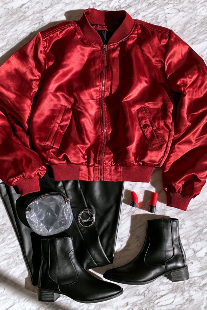 Red bomber jacket and black leather pants with a clear clutch on white marble