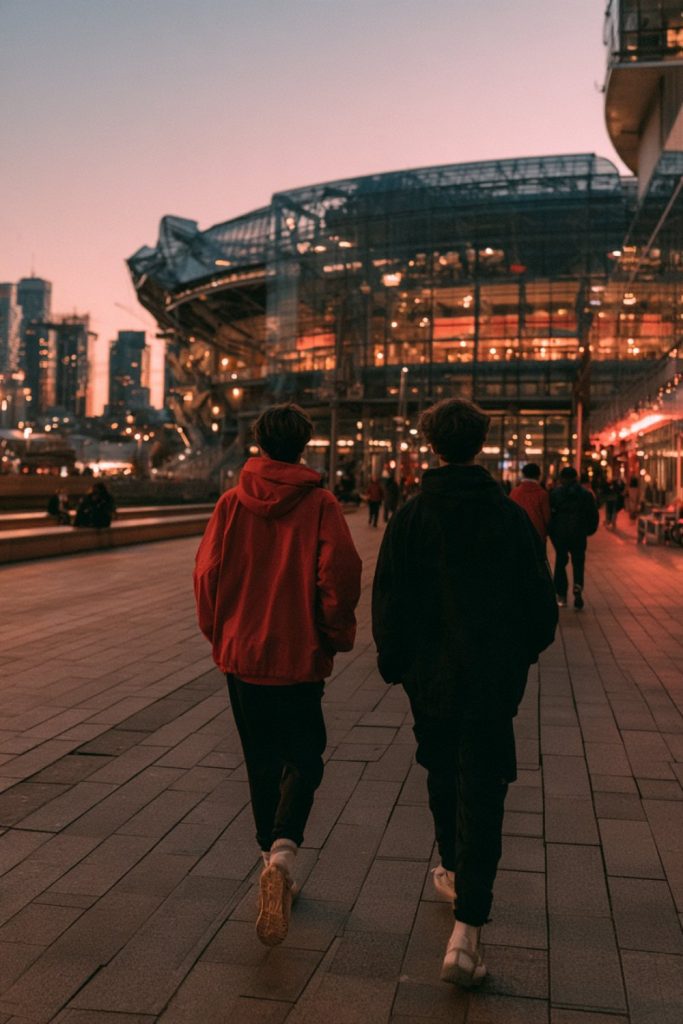 Fans in red and black seen from behind crossing a plaza toward the stadium as city lights come on