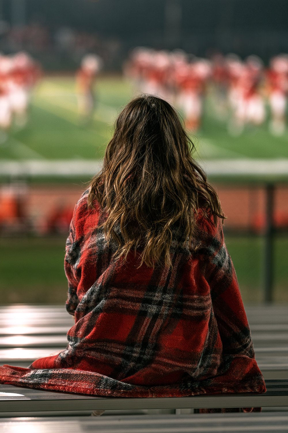 Football parent wrapped in a plaid blanket on the bleachers during a night game