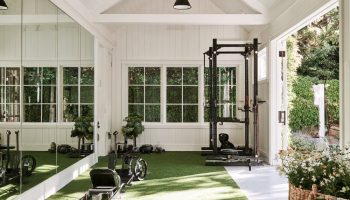Bright white garage gym with a large mirror, a green turf strip, kettlebells and a squat rack