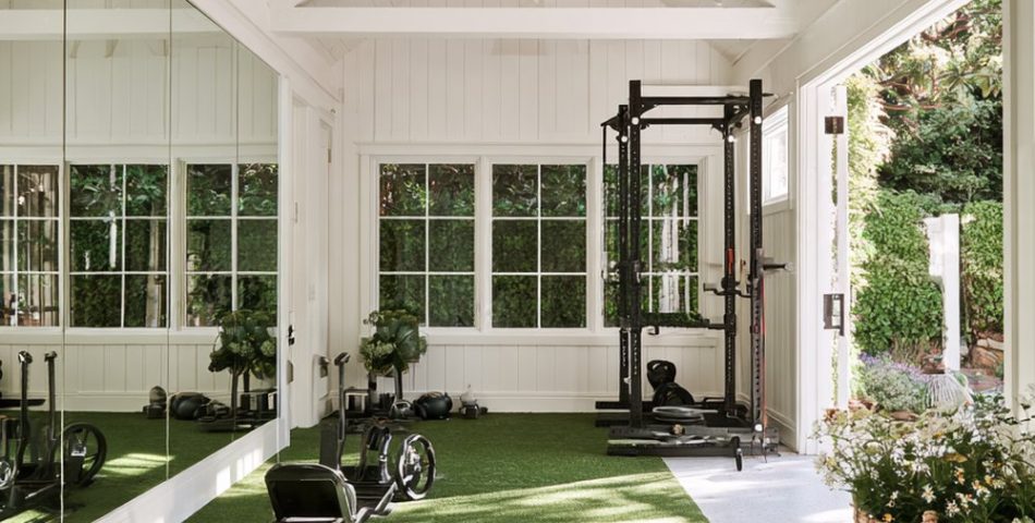 Bright white garage gym with a large mirror, a green turf strip, kettlebells and a squat rack