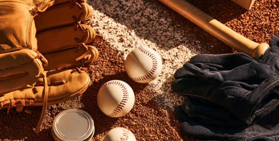Flat lay on infield dirt of a leather baseball glove, baseballs, wooden bat, batting gloves and a wrapped gift
