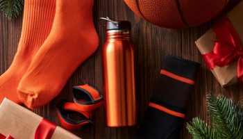 Gifts for basketball players flat lay with a basketball, orange crew socks, water bottle, sweatbands and wrapped gifts with pine