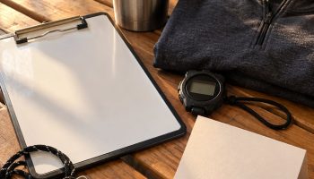 Flat lay of coach gifts on a locker room bench: whistle, clipboard, tumbler, stopwatch and quarter zip