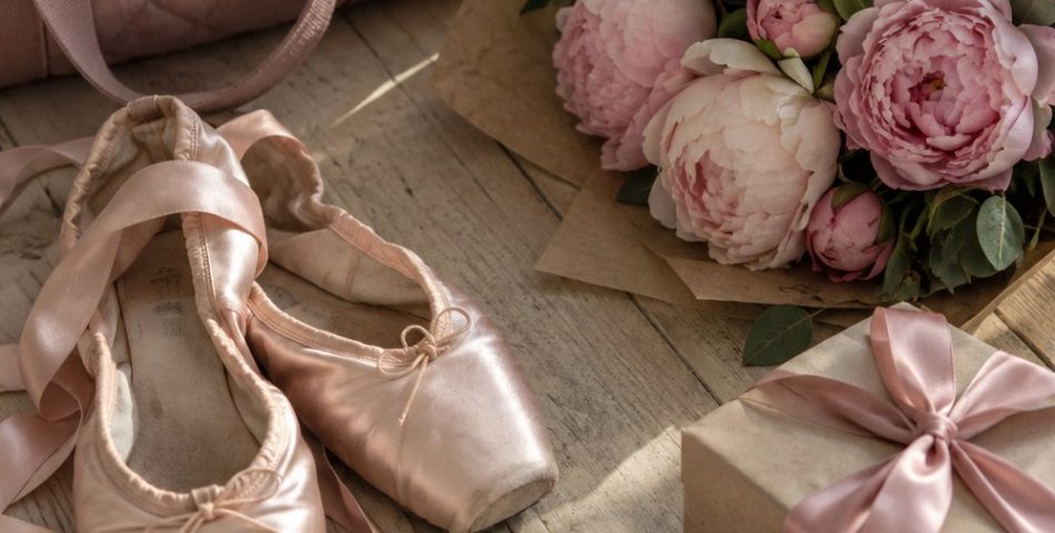 Flat lay of pink satin ballet slippers, a peony bouquet in kraft paper, a quilted dance bag, bobby pins and a gift box with a satin bow