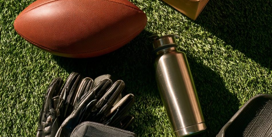 Flat lay on turf of a football, receiver gloves, mouthguard case, foam roller, water bottle, slides and a wrapped gift