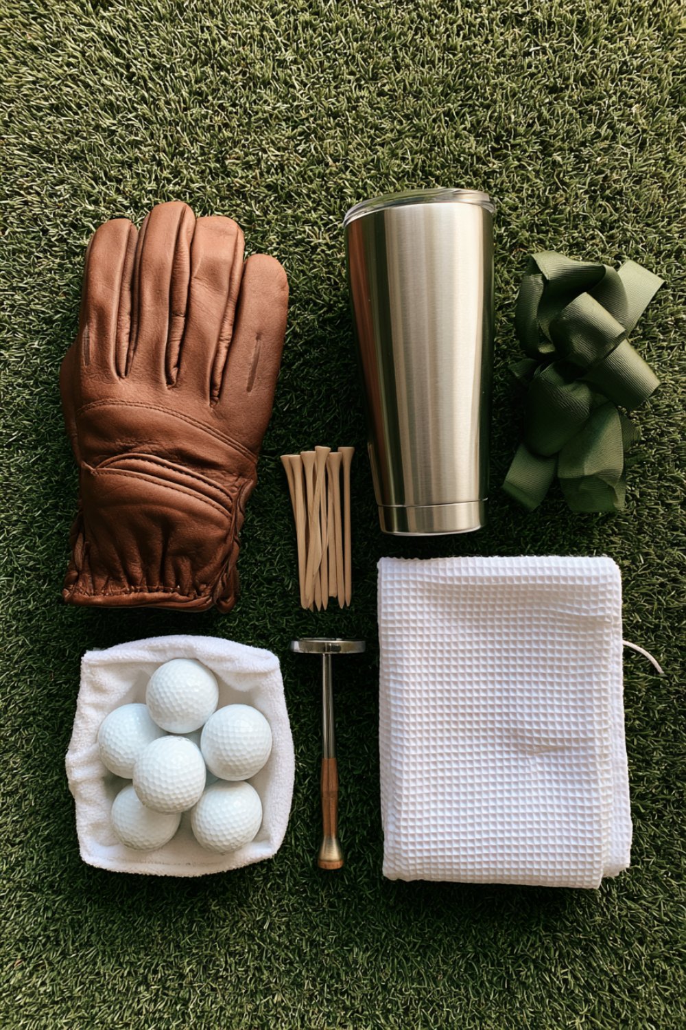 Golf gift flat lay with a leather glove, white balls in a box, tees, a towel and an insulated tumbler
