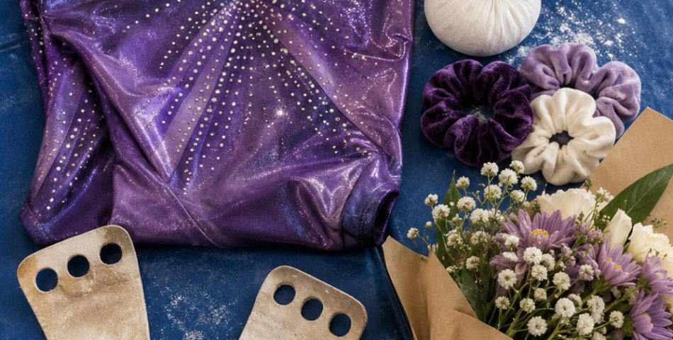 Flat lay on a blue gymnastics mat with a sparkly purple leotard, leather grips, a chalk ball, scrunchies, a water bottle and a small bouquet