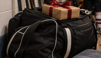 Hockey bag on a locker room bench with a wrapped gift, stick tape, skate guards and a puck