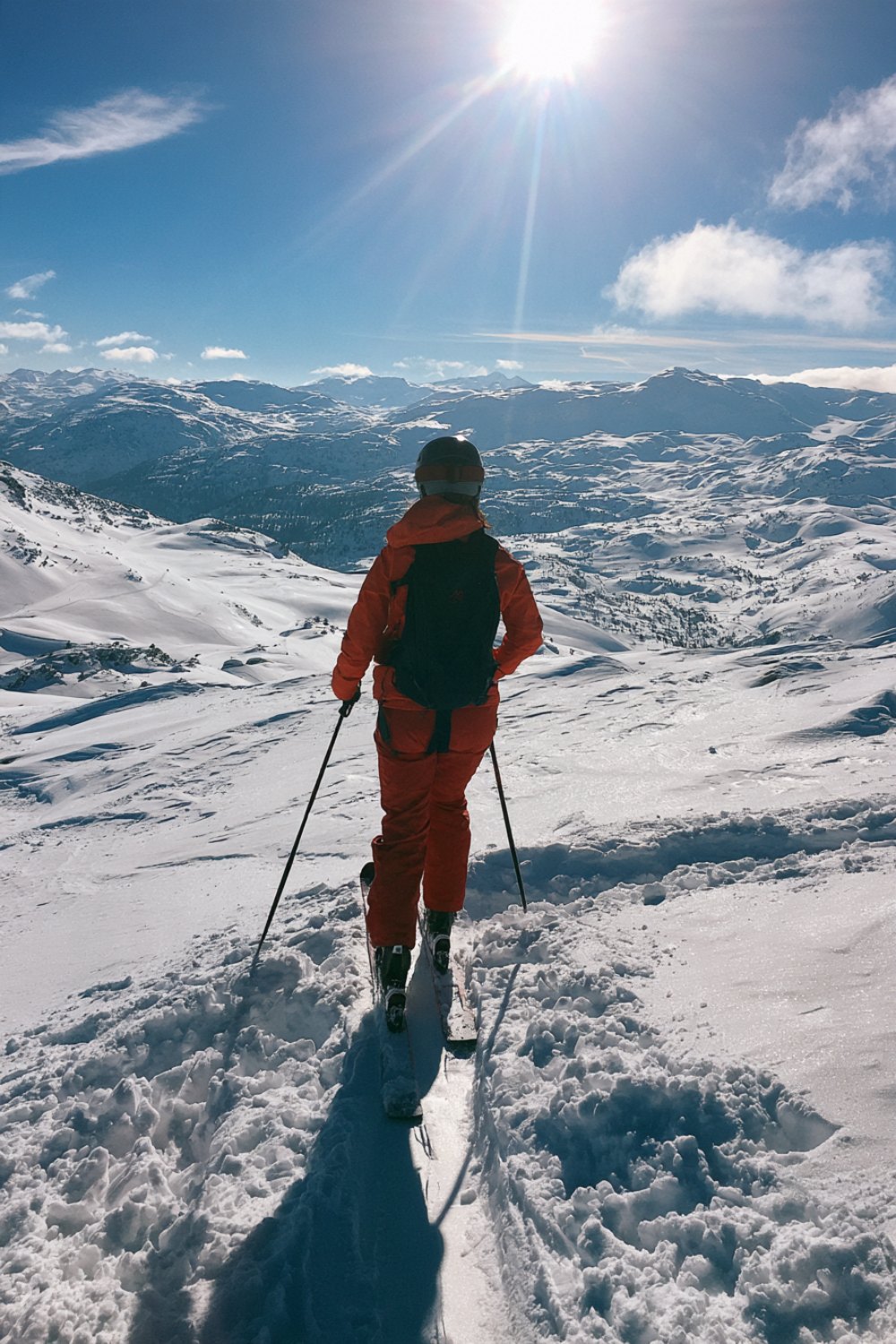 Skier seen from behind at the top of a sunny slope looking over the mountains
