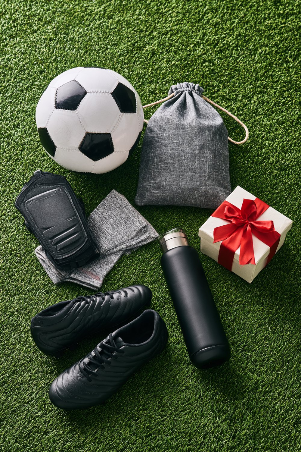 Soccer ball, gray drawstring bag, shin guards, grip socks, black cleats and a water bottle laid out as gift ideas