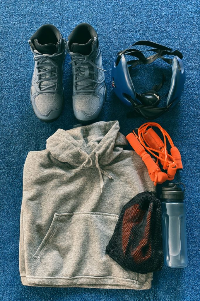 Flat lay of wrestler gifts: high-top wrestling shoes, ear guards, grey hoodie, jump rope and water bottle