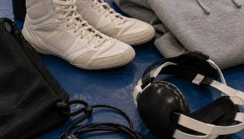 Flat lay on a blue wrestling mat of wrestling shoes, ear guard headgear, hoodie, jump rope and shoe bag