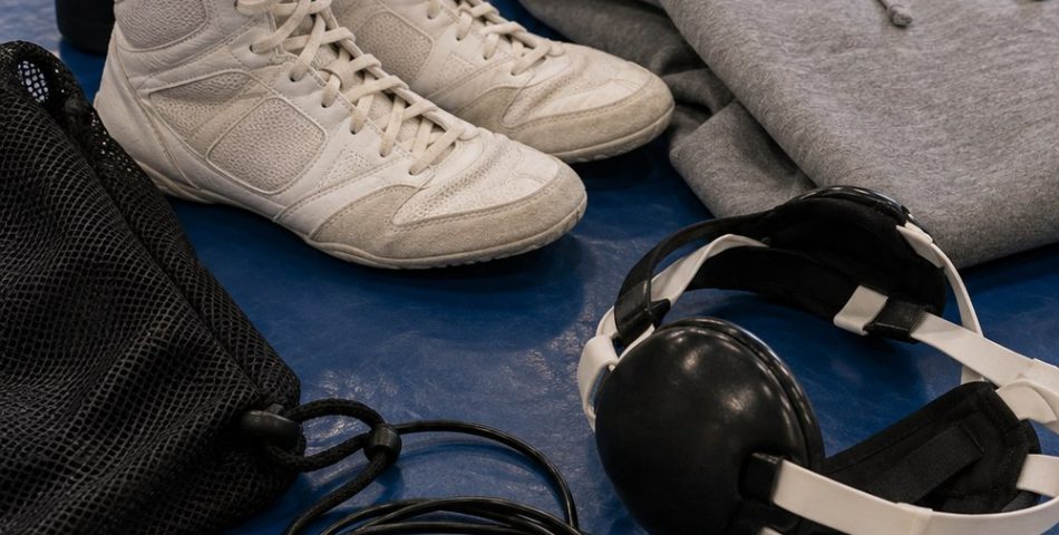 Flat lay on a blue wrestling mat of wrestling shoes, ear guard headgear, hoodie, jump rope and shoe bag