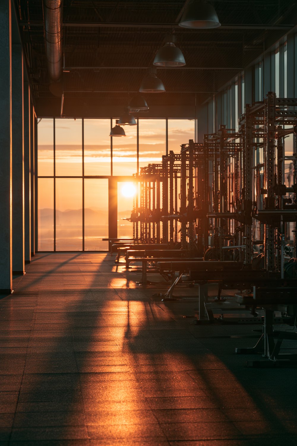 Rows of squat racks in an empty gym with golden sunrise light across the floor