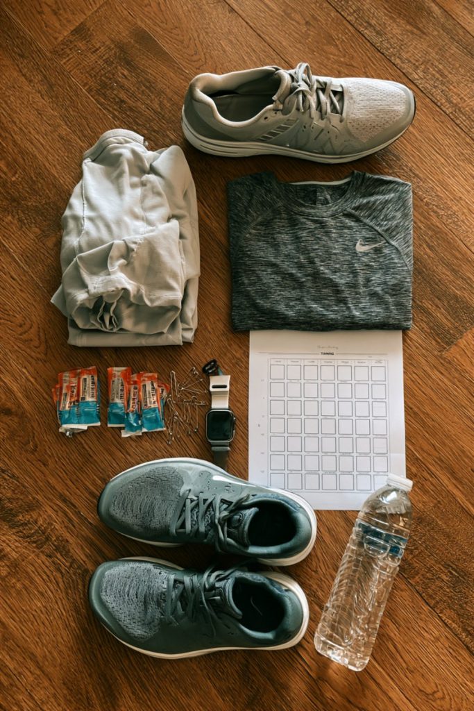 Flat lay of half marathon prep: running shoes, long sleeve top, gels, safety pins, watch and a blank training calendar