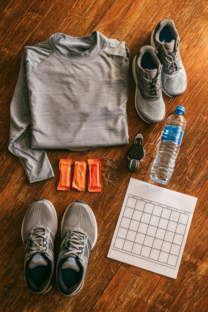 Race week kit laid out on a wooden floor with shoes, a water bottle and a paper calendar